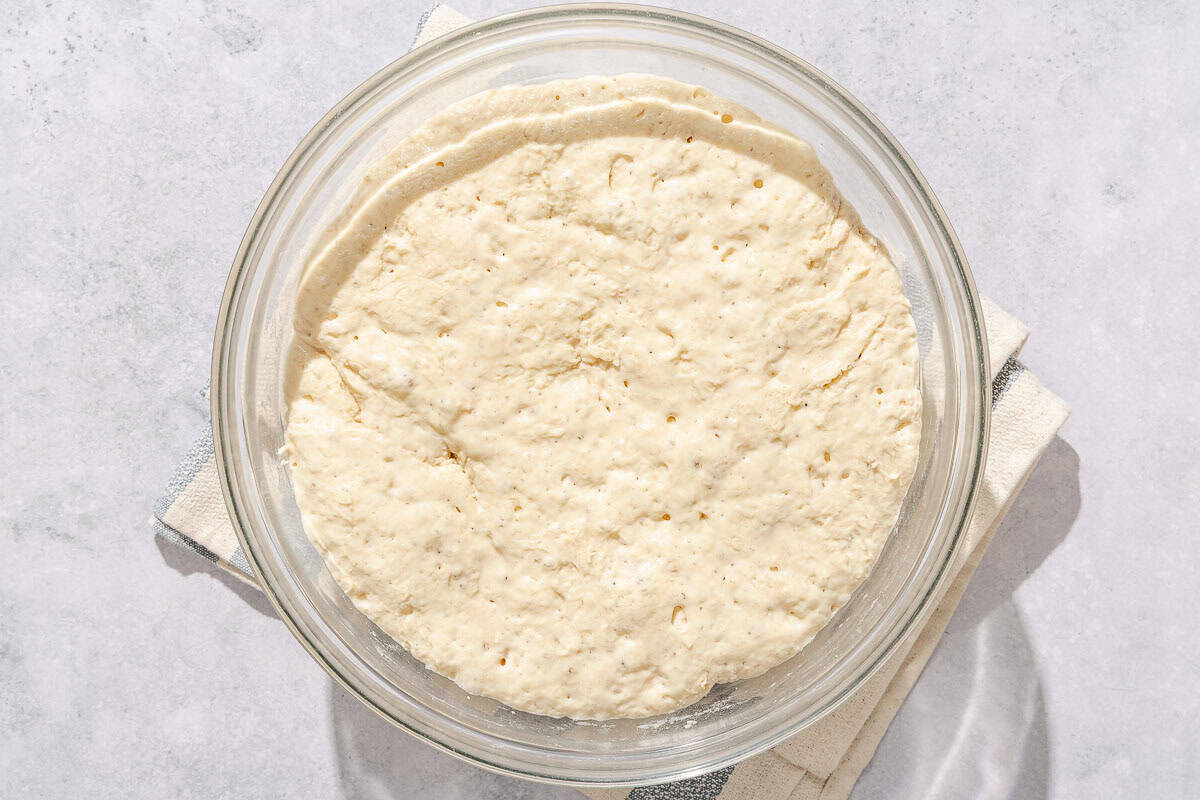 Risen dough for baguette in a glass bowl resting on a kitchen towel.