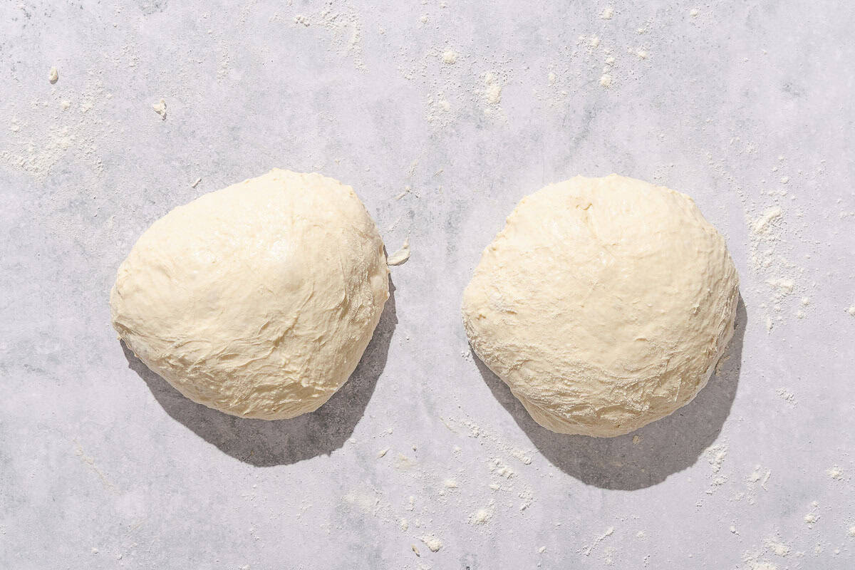 Two balls of dough resting on a countertop dusted in flour.