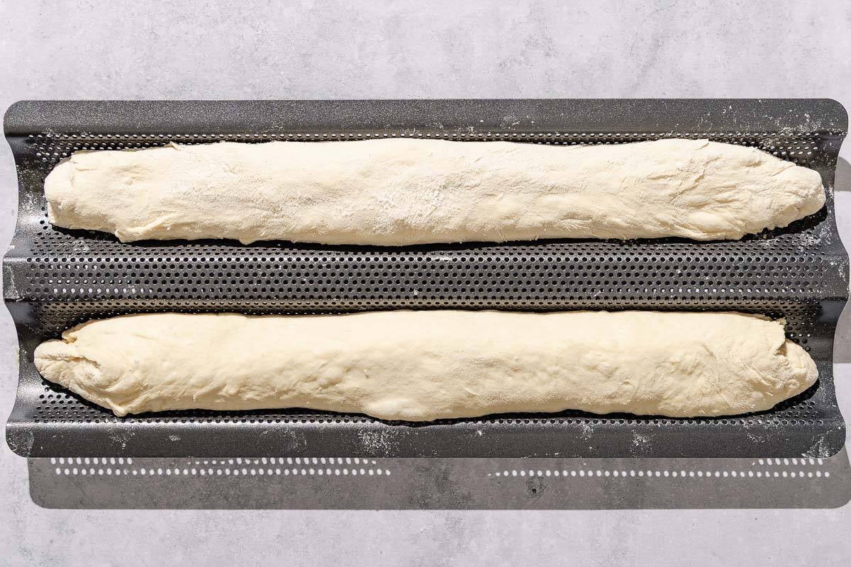 Two unbaked French baguettes on a wire rack.