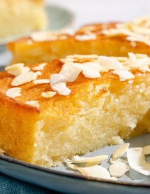 A close up of a slice of the basbousa on a platter with the rest of the cake.