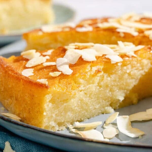 A close up of a slice of the basbousa on a platter with the rest of the cake.