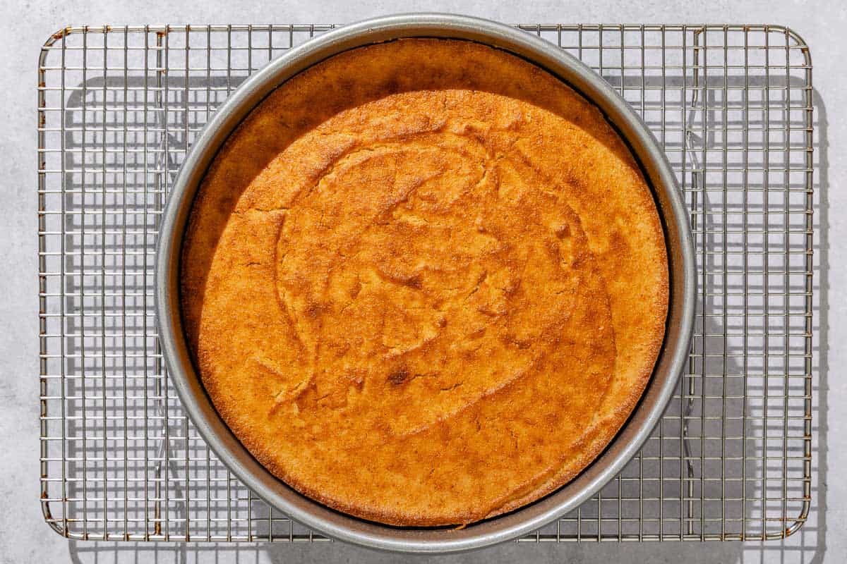 The baked basbousa in a round cake pan cooling on a wire rack.