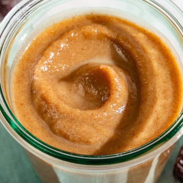 Date Caramel in a jar sitting on a cloth napkin surrounded by some dates and a spoon.