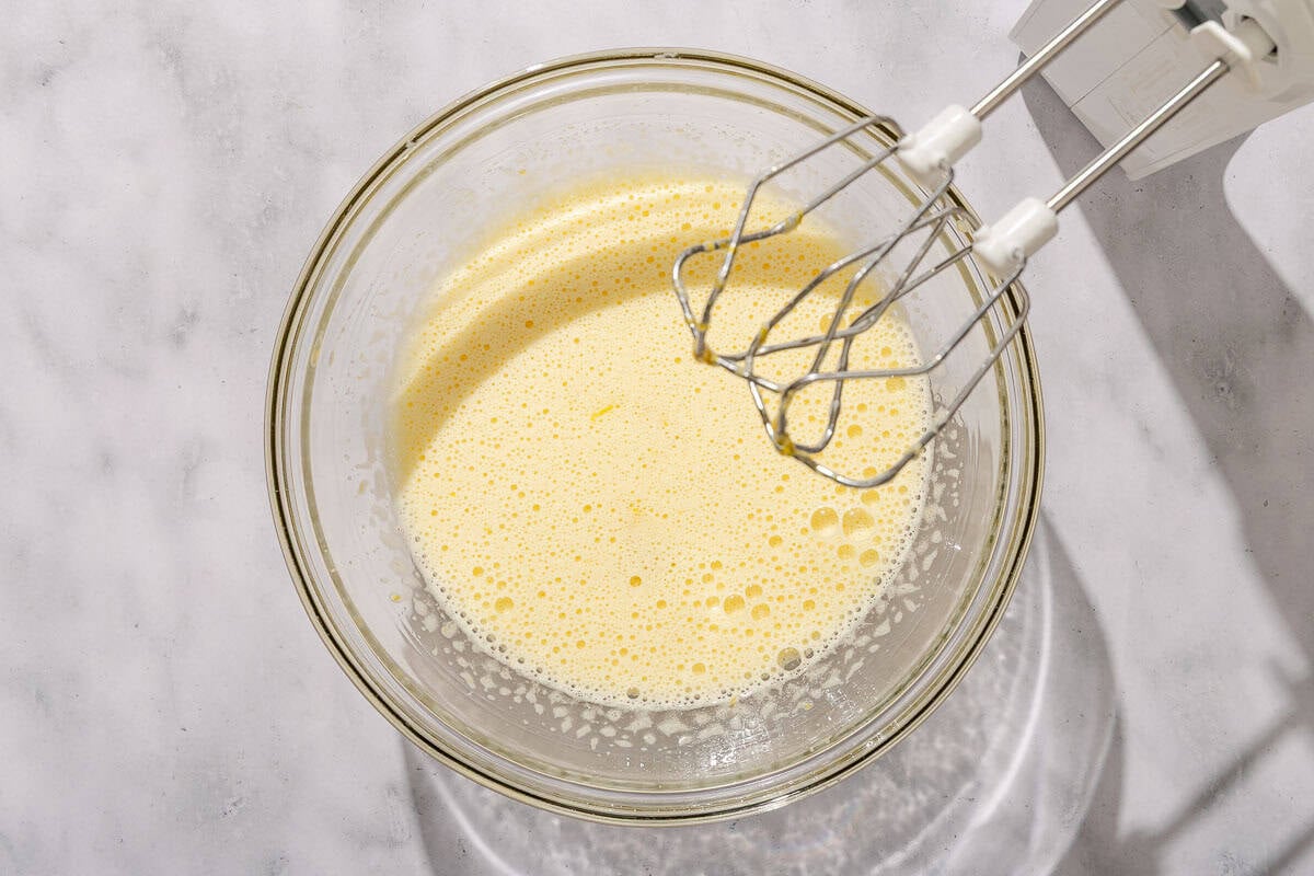 The mixture of eggs for the lemon pudding in a bowl with a hand mixer next to it.
