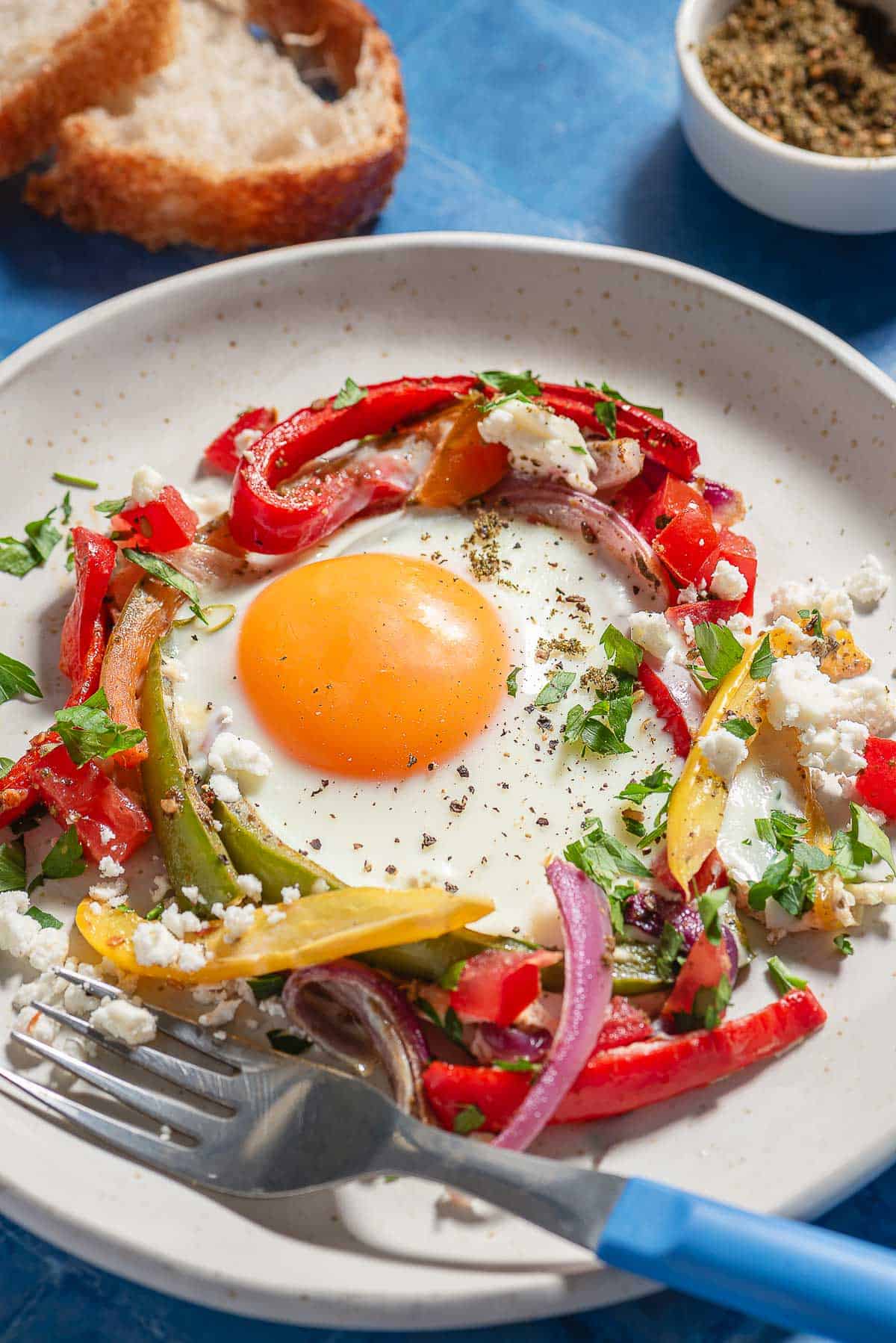 A serving of the sheet pan eggs on a plate with a fork next to 2 slices of bread and bowls of za'atar and aleppo pepper.