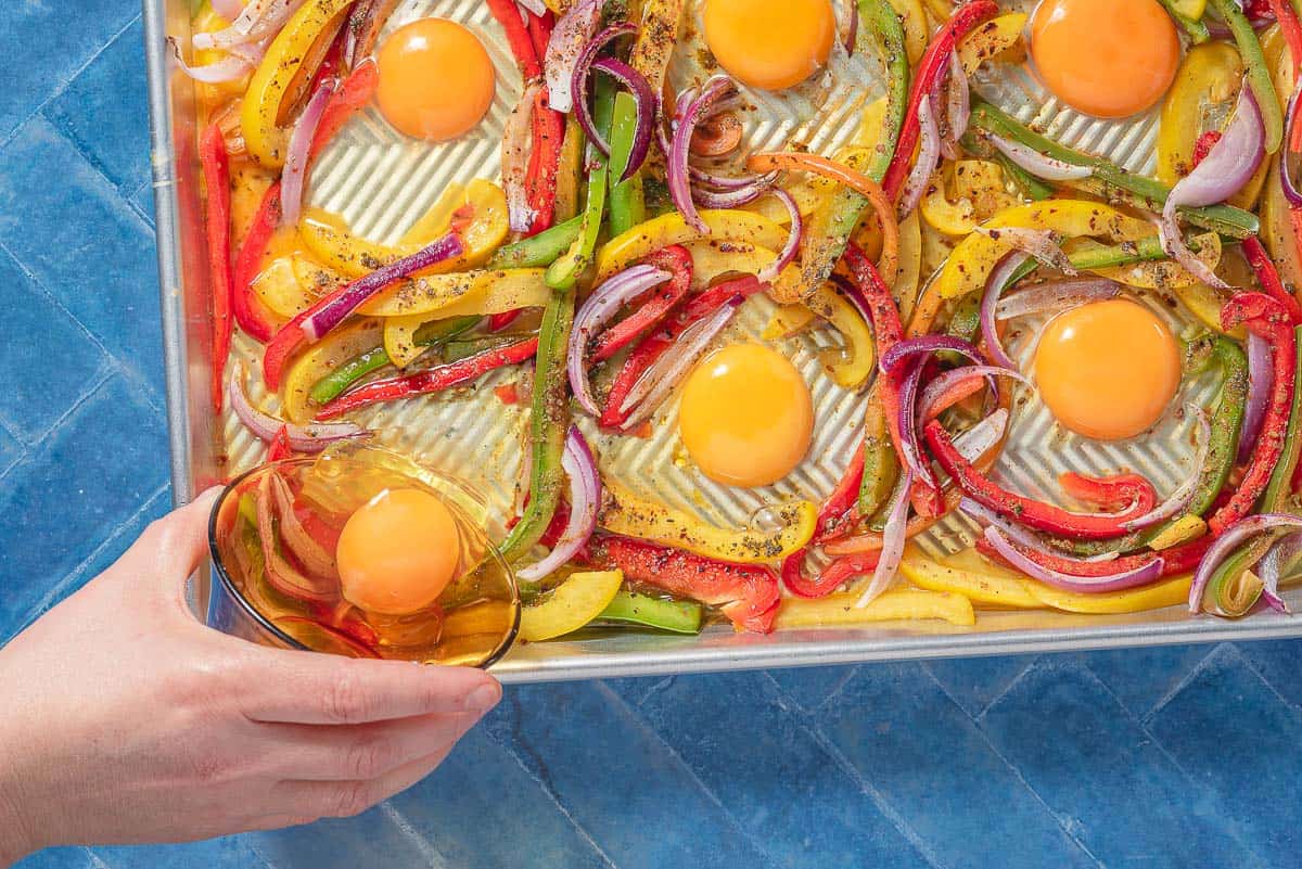The 6 eggs being nestled into the roasted vegetables on the sheet pan.