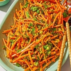Carrot salad with herbs on a platter with serving utensils next to a bowl of the dressing.