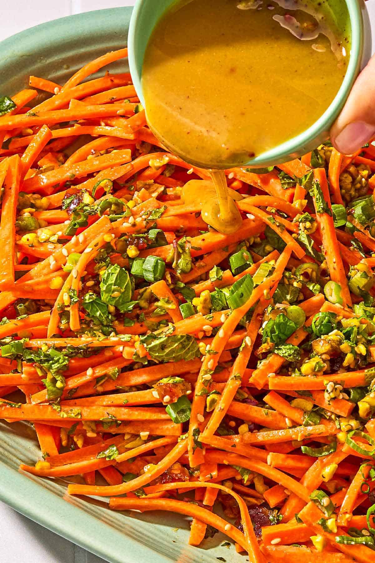 The dressing being poured on the carrot salad with herbs.