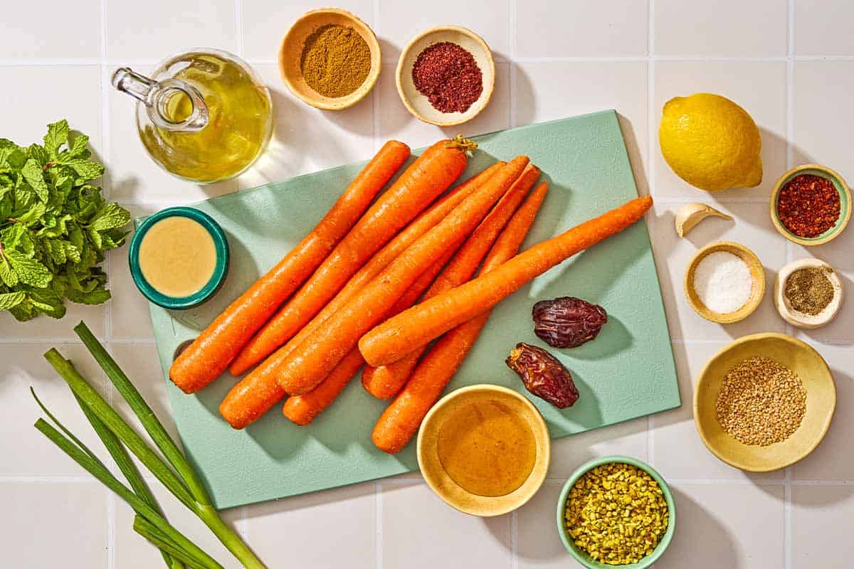 Ingredients for carrot salad with herbs including carrots, lemon, garlic, tahini, honey, water, sumac, cumin, Aleppo pepper, salt, black pepper, and olive oil.