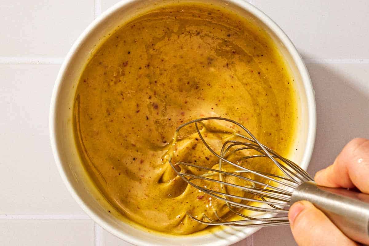 The dressing for the carrot salad with herbs in a bowl being stirred with a whisk.