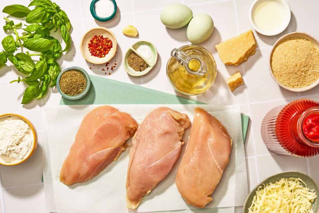 Ingredients for the chicken parmesan recipe including chicken breasts, olive oil, garlic, red pepper flakes, salt, sugar, tomato passata, basil, flour, eggs, breadcrumbs, grated parmigiano-reggiano cheese, italian seasoning, and shredded mozzarella.