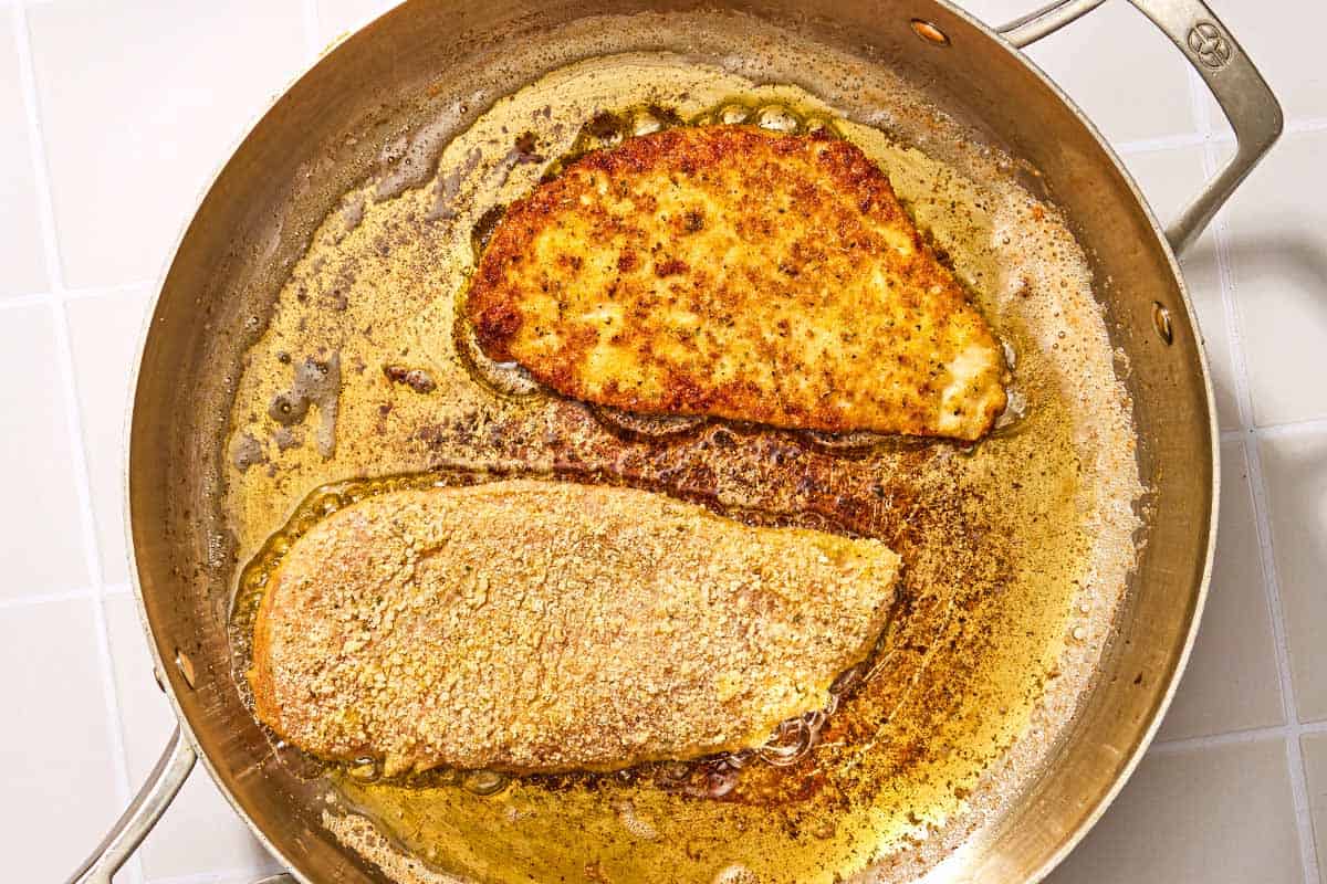 Breaded chicken cutlets being fried in oil in a skillet.