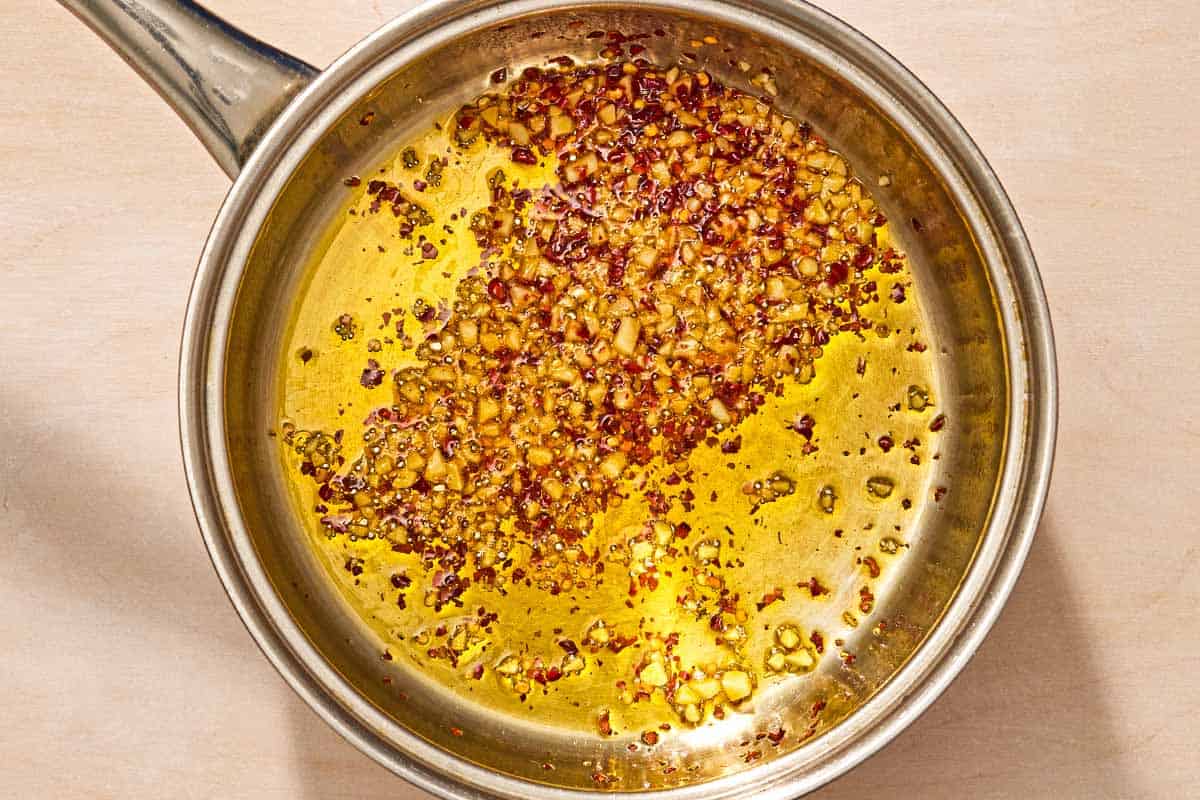 Chopped garlic and red pepper flakes heating in garlic in a saucepan.
