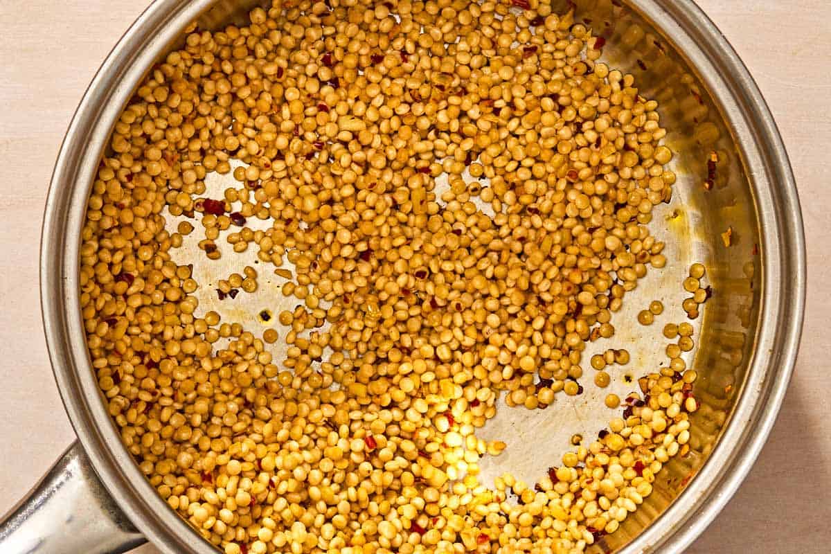 Couscous being tossed with the olive oil, red pepper flakes and garlic in the saucepan.