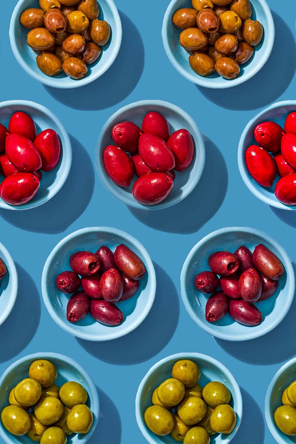 Several small bowls with various variety of olives placed evenly in rows.