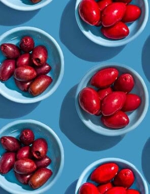 Several small bowls with various variety of olives placed evenly in rows.