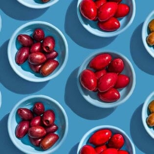 Several small bowls with various variety of olives placed evenly in rows.