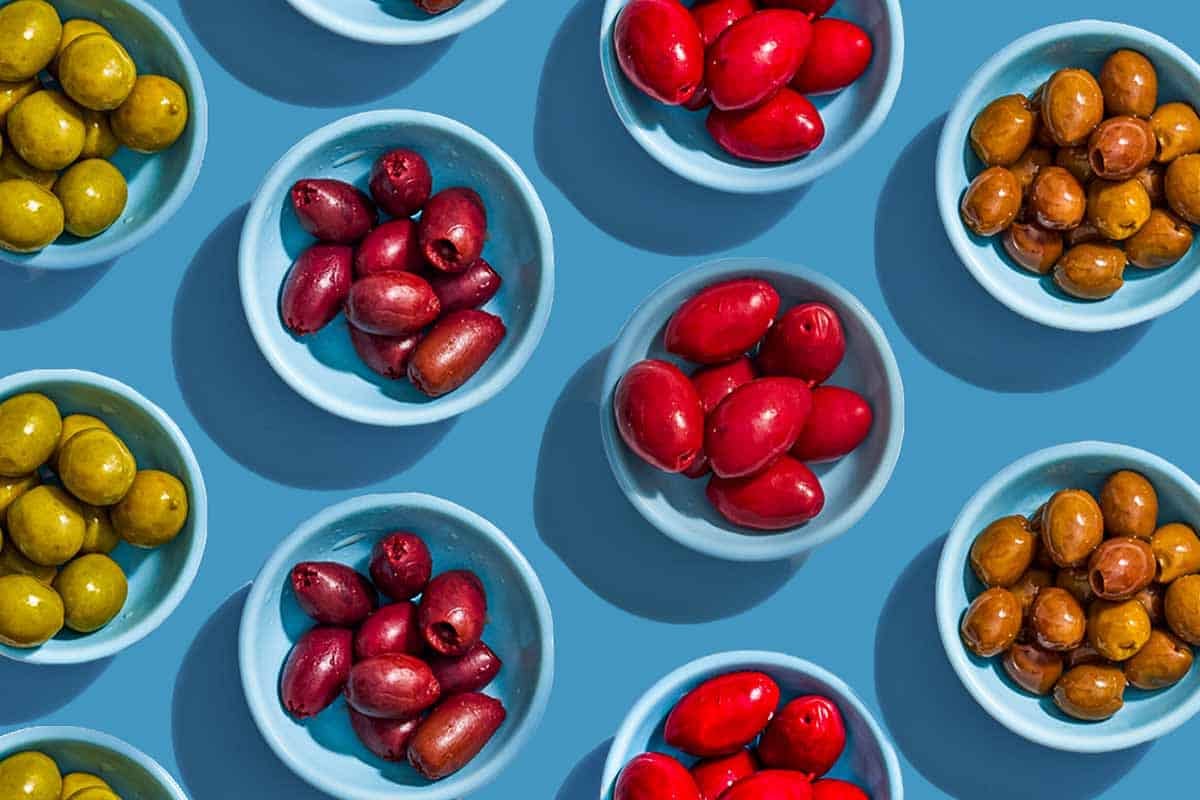 Several small bowls with various variety of olives placed evenly in rows.