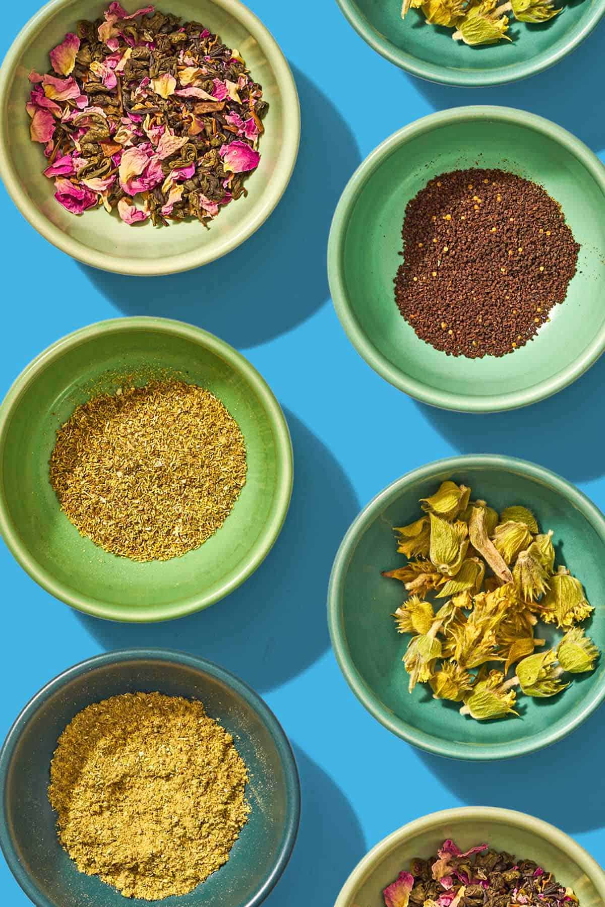 7 bowls containing various different flavored tea leaves.