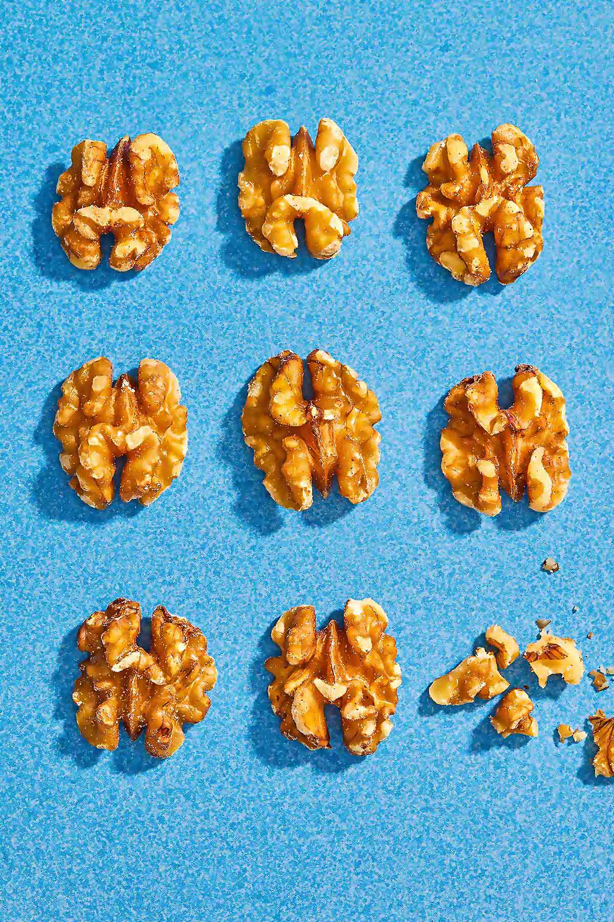 9 walnuts evenly placed on a blue background with one crushed into crumbs.