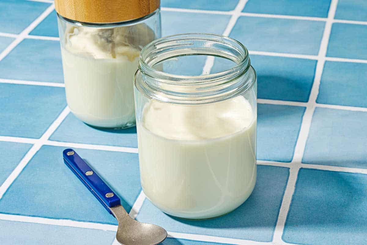 The strained yogurt in 2 jars next to a spoon.