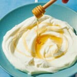 A bowl of homemade greek yogurt being drizzled with honey from a honey dipper.