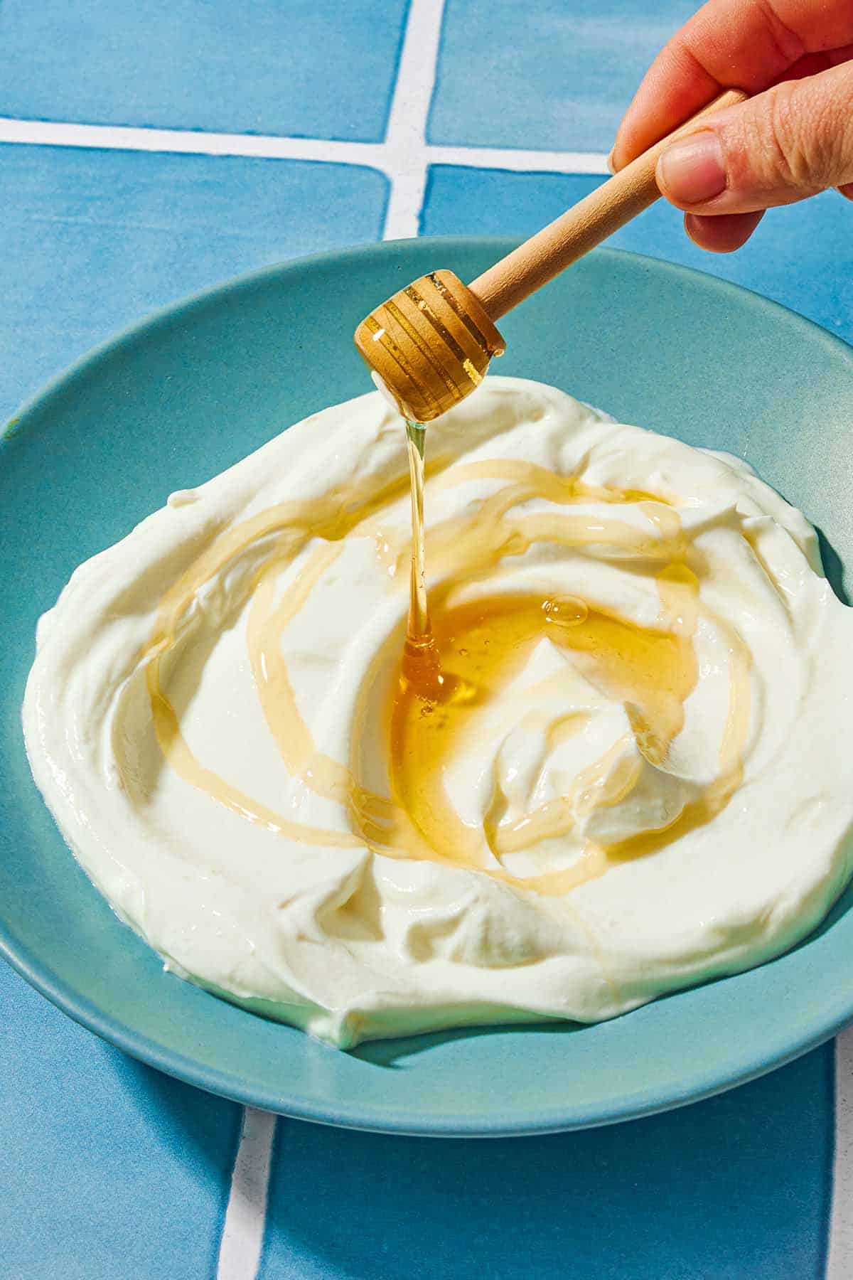 A bowl of homemade greek yogurt being drizzled with honey from a honey dipper.