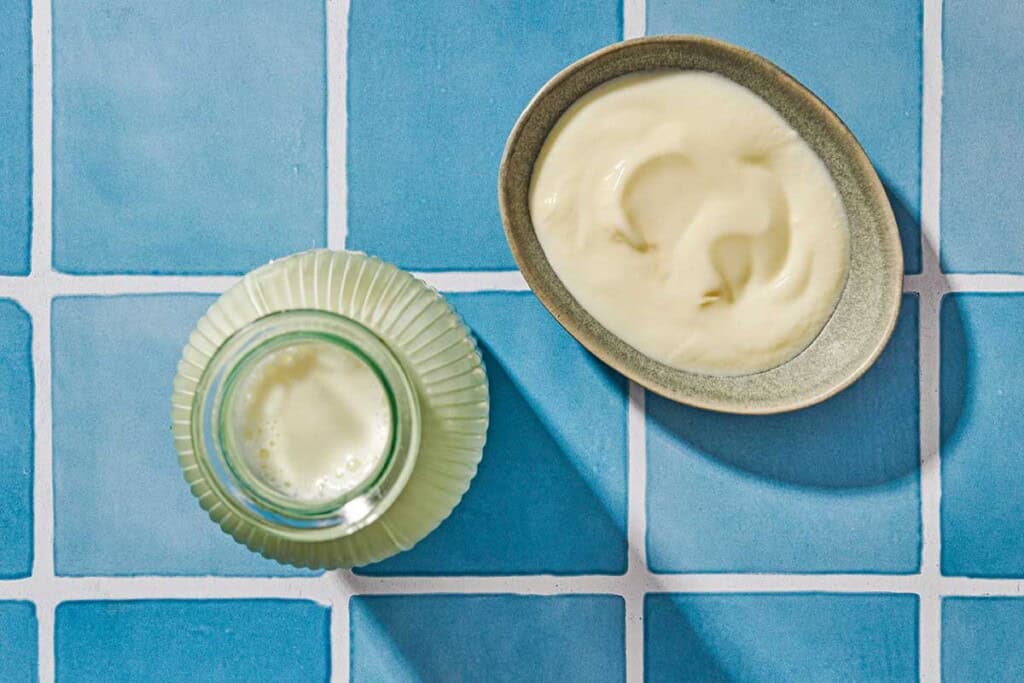 A small bowl of yogurt next to a small jar of milk.
