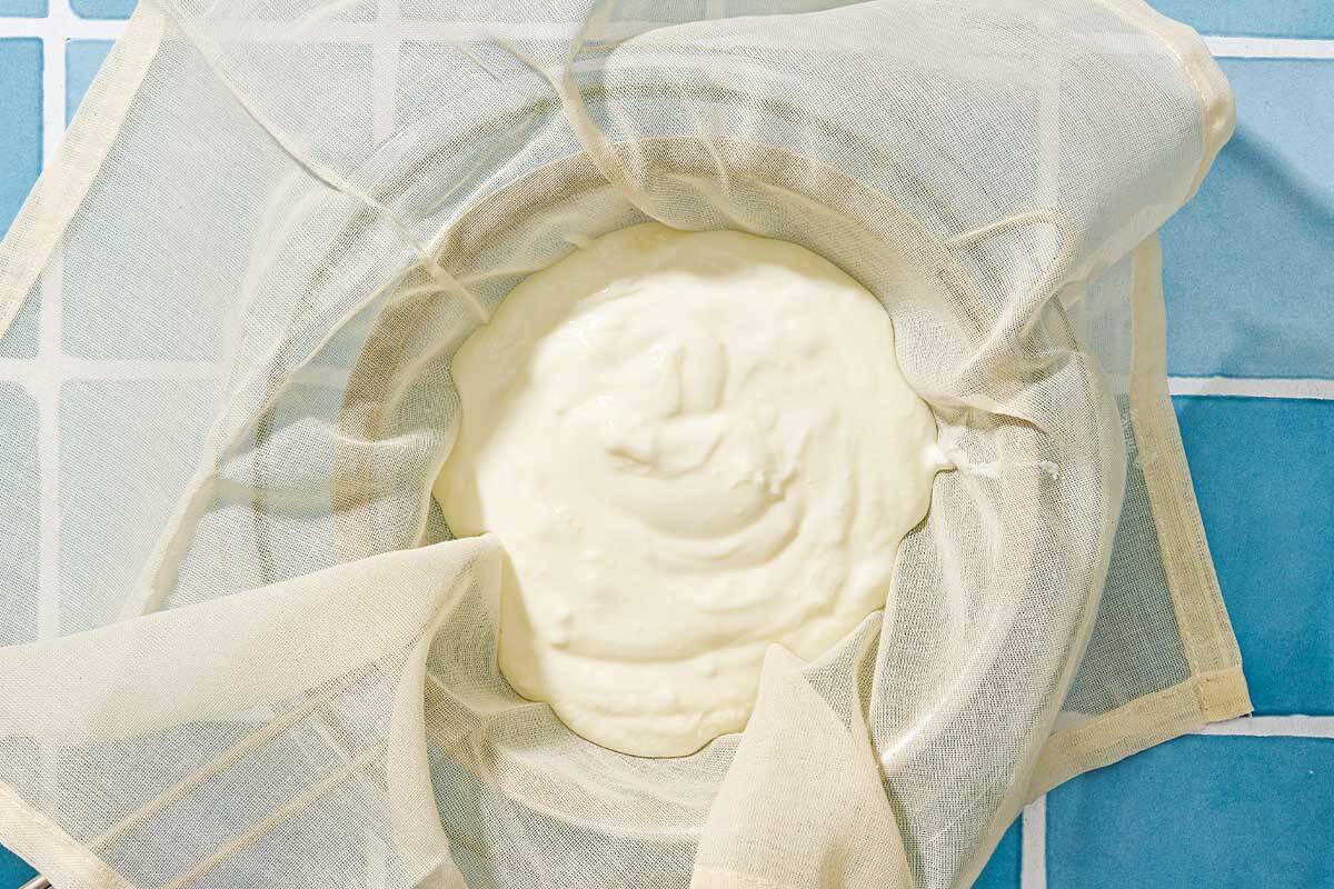 The homemade greek yogurt being strained in cheesecloth over a bowl.