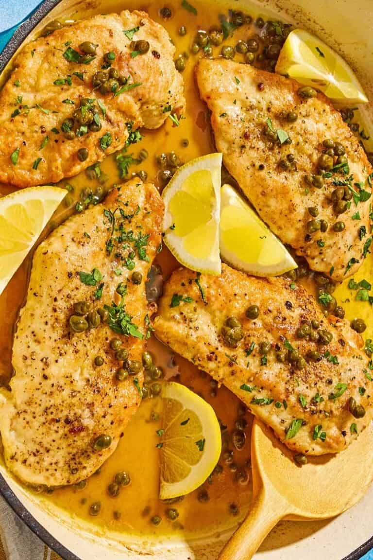 Chicken piccata with lemon wedges in a skillet with a wooden spoon.