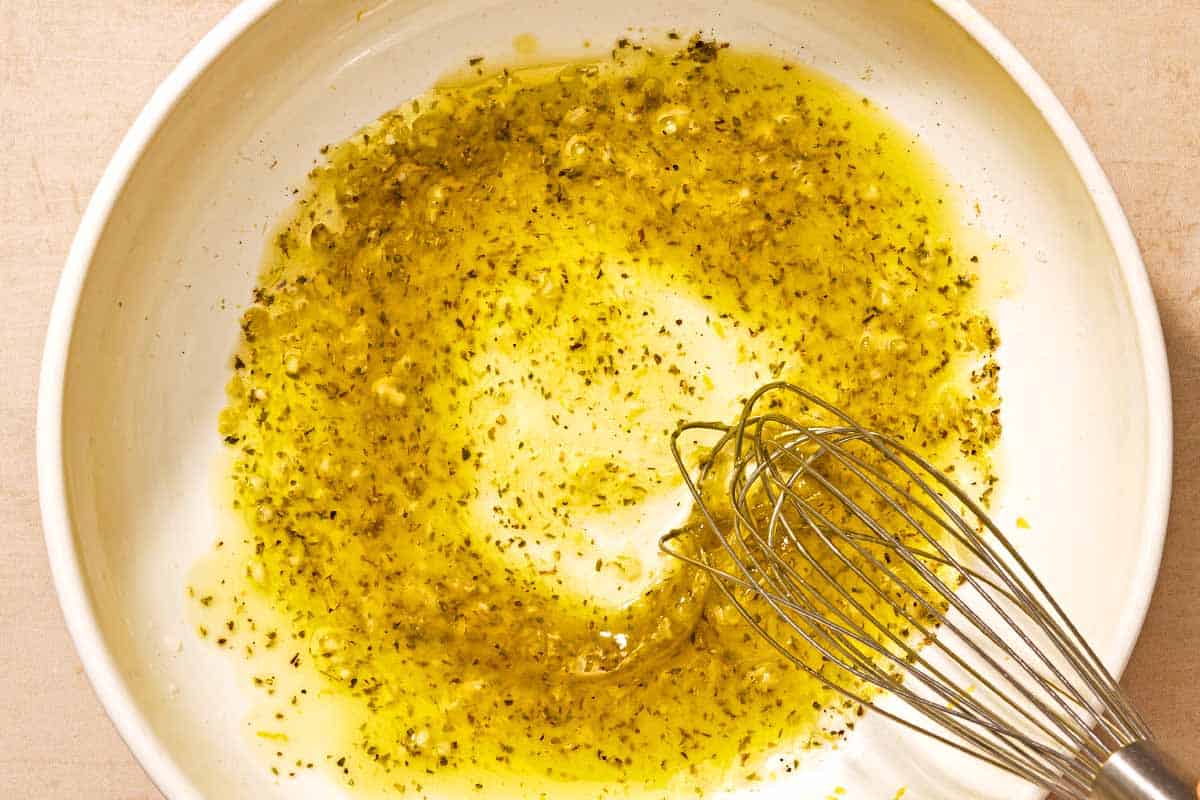 The dressing for the arugula salad in a bowl with a whisk.