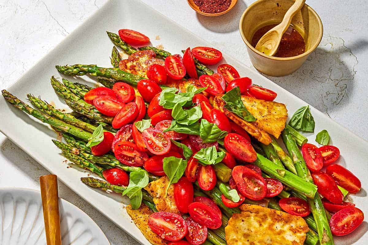 Roasted Asparagus Salad with Fried Halloumi and Fresh Tomatoes on a serving platter next to bowls of sumac and the sherry vinaigrette.