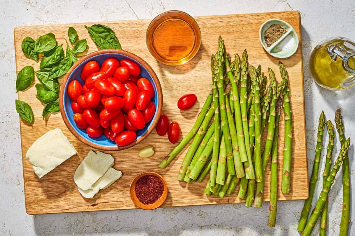 Ingredients for roasted asparagus salad including asparagus, grape tomatoes, halloumi, olive oil, salt, black pepper, basil, sherry vinegar, garlic, and sumac.