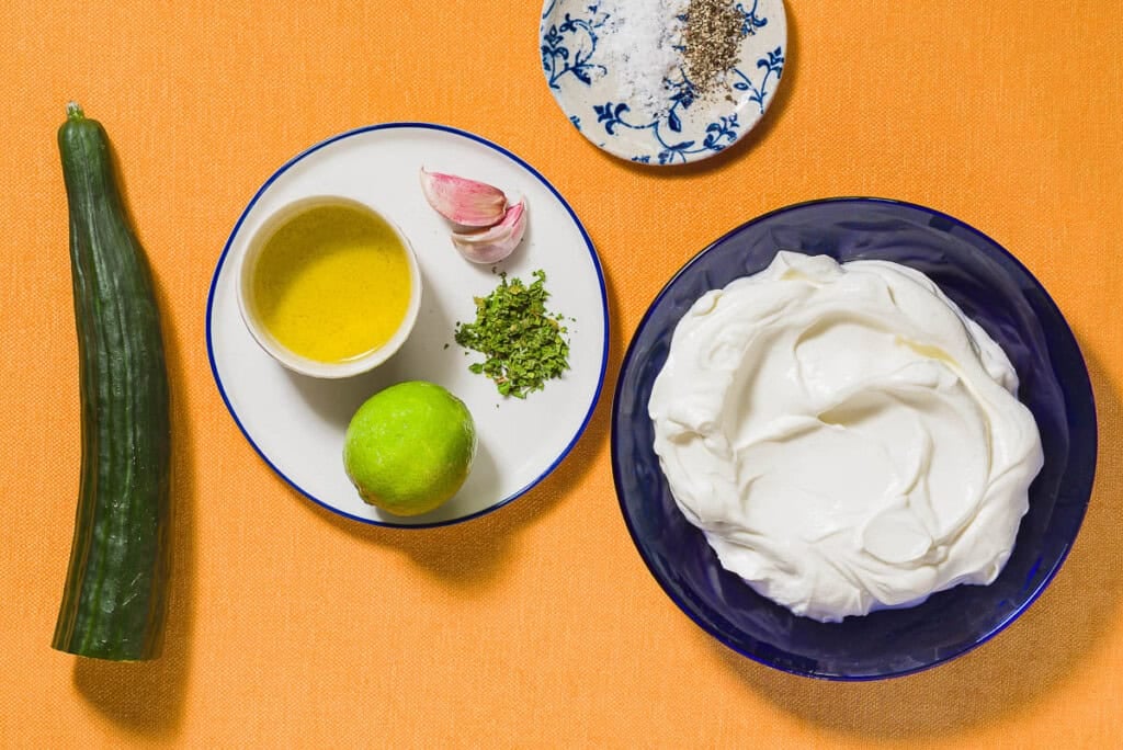 Ingredients for Maast O'Khiar including greek yogurt, cucumber, garlic, dried mint, lime, olive oil, salt, black pepper.