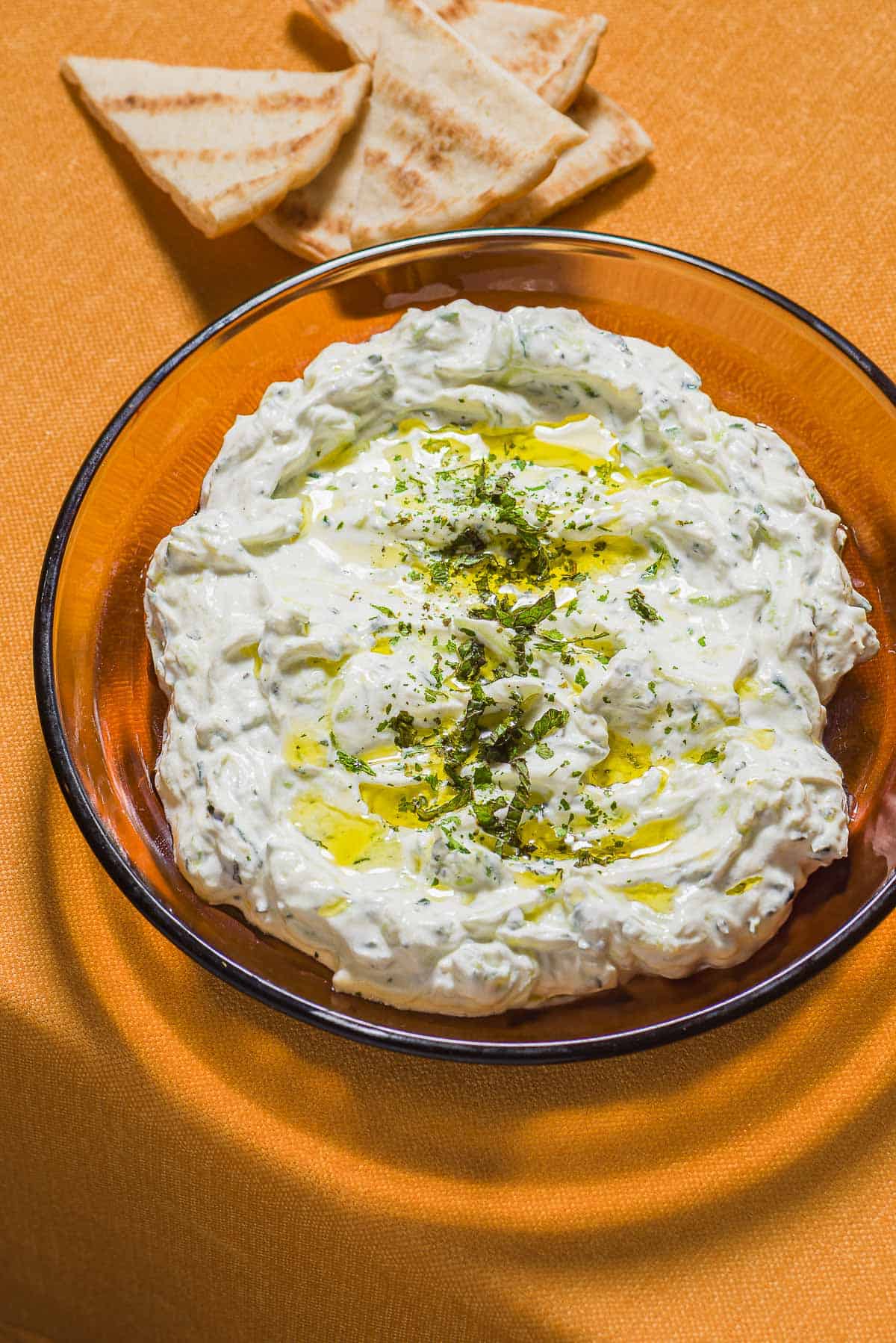 Maast O'Khiar garnished with dried mint and a drizzle of olive oil in a bowl next to some pita wedges.