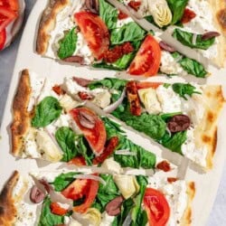 Slices of the flatbread pizza on a platter surrounded by bowls of kalamata olives, oregano and sliced tomato.