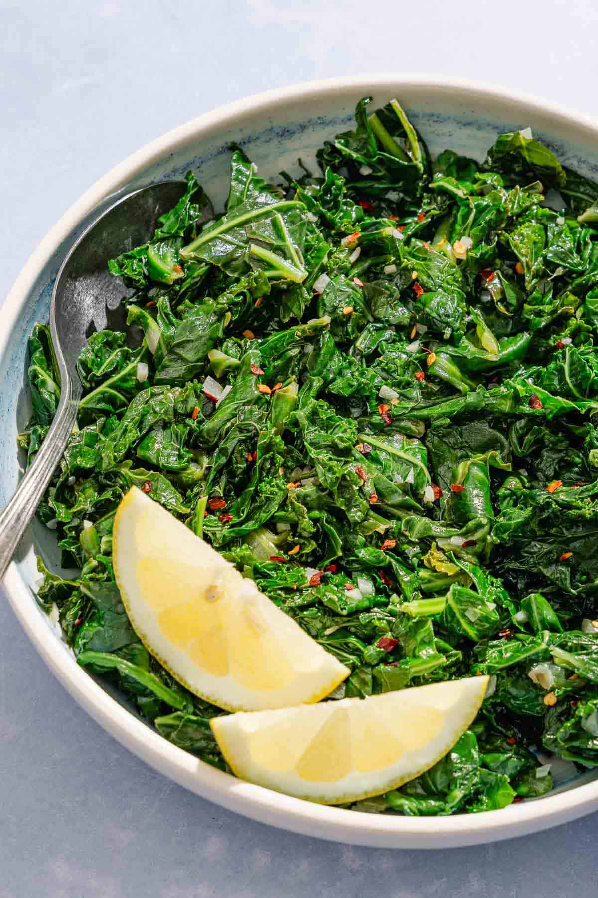 Horta in a serving bowl with 2 lemon wedges and a spoon.