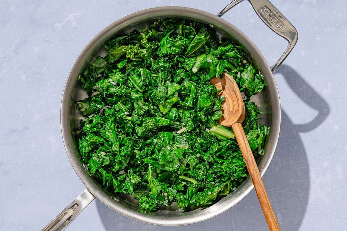 The greens for the horta being sauteed in a deep skillet with a wooden spoon.