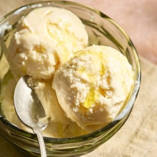 Scoops of olive oil ice cream topped with flaky sea salt and a drizzle of olive oil in a bowl with a spoon.