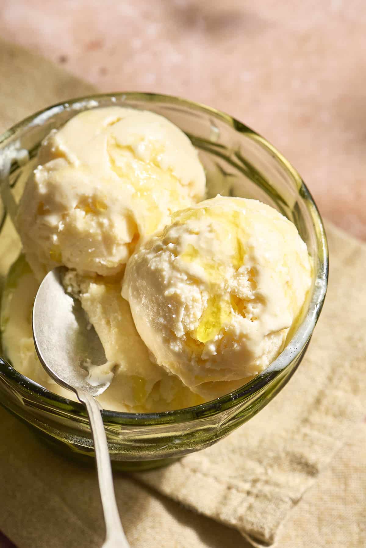 Scoops of olive oil ice cream topped with flaky sea salt and a drizzle of olive oil in a bowl with a spoon.