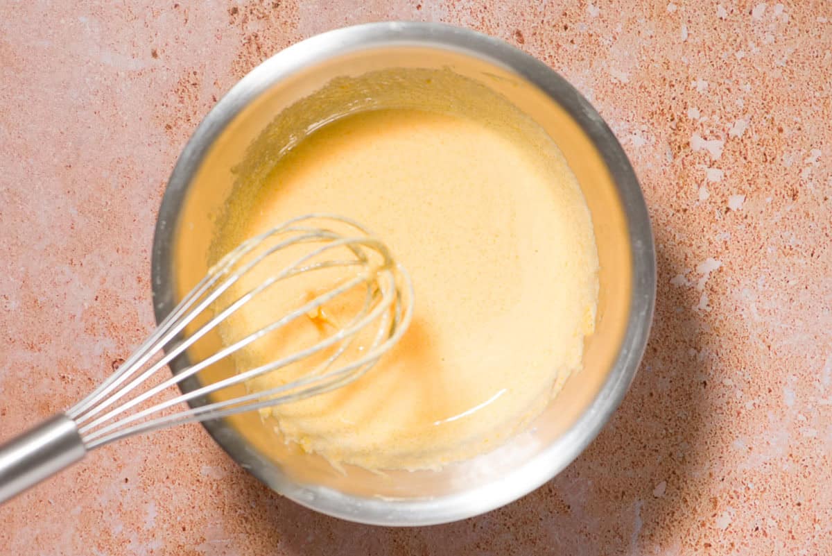 The eggs for the olive oil ice cream mixture being tempered in a bowl with a whisk.