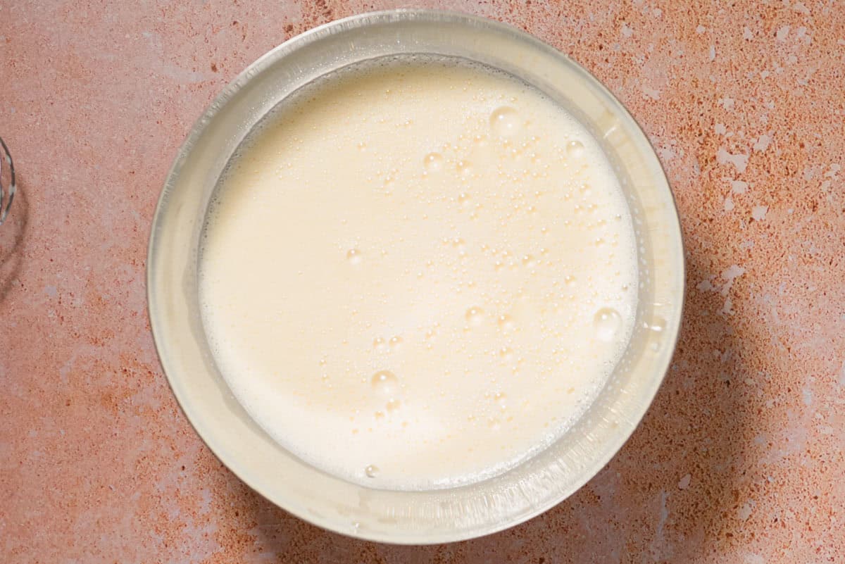 The strained olive oil ice cream mixture in a glass container before being places in a the refrigerator.