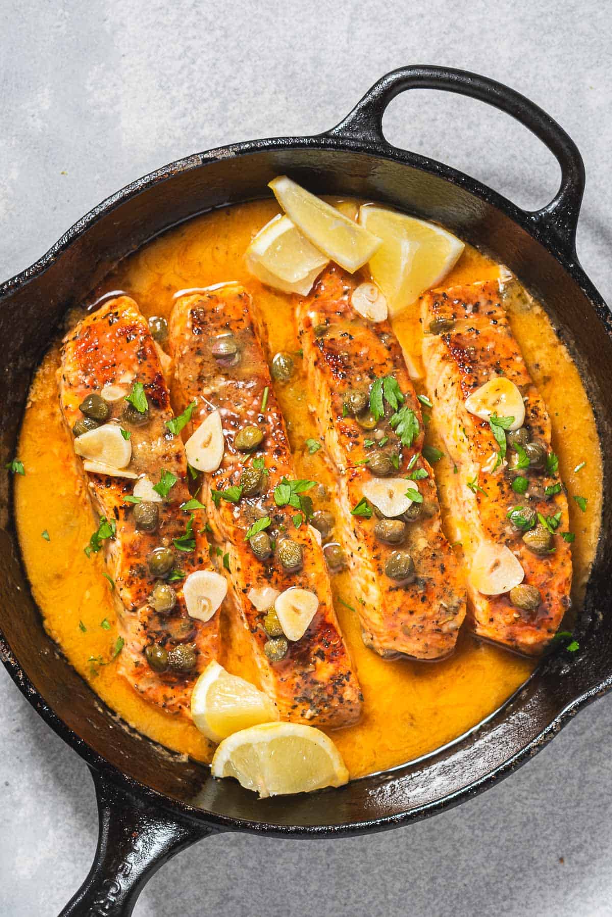 4 salmon piccata fillets along with the sauce in a cast iron skillet with lemon wedges.