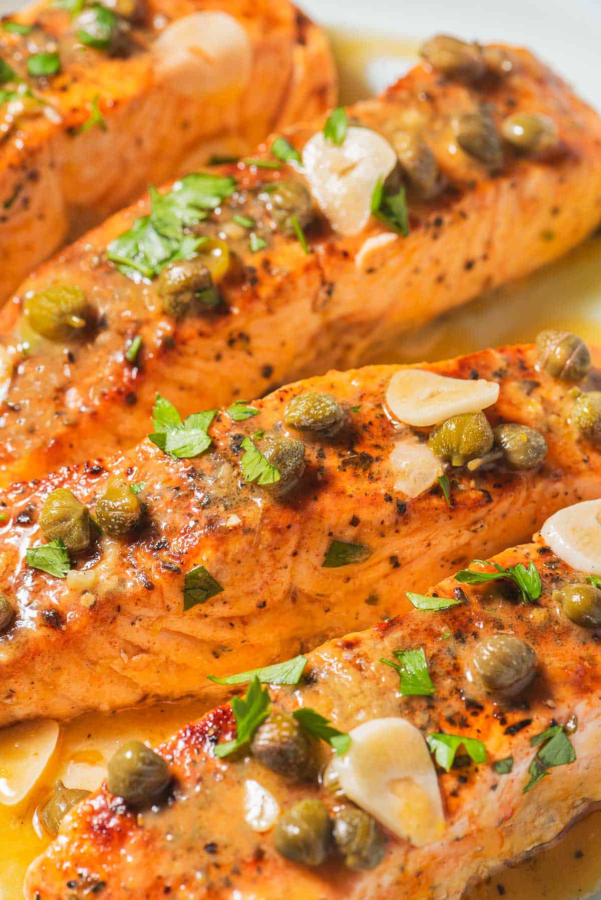 A close up of 4 salmon piccata fillets.