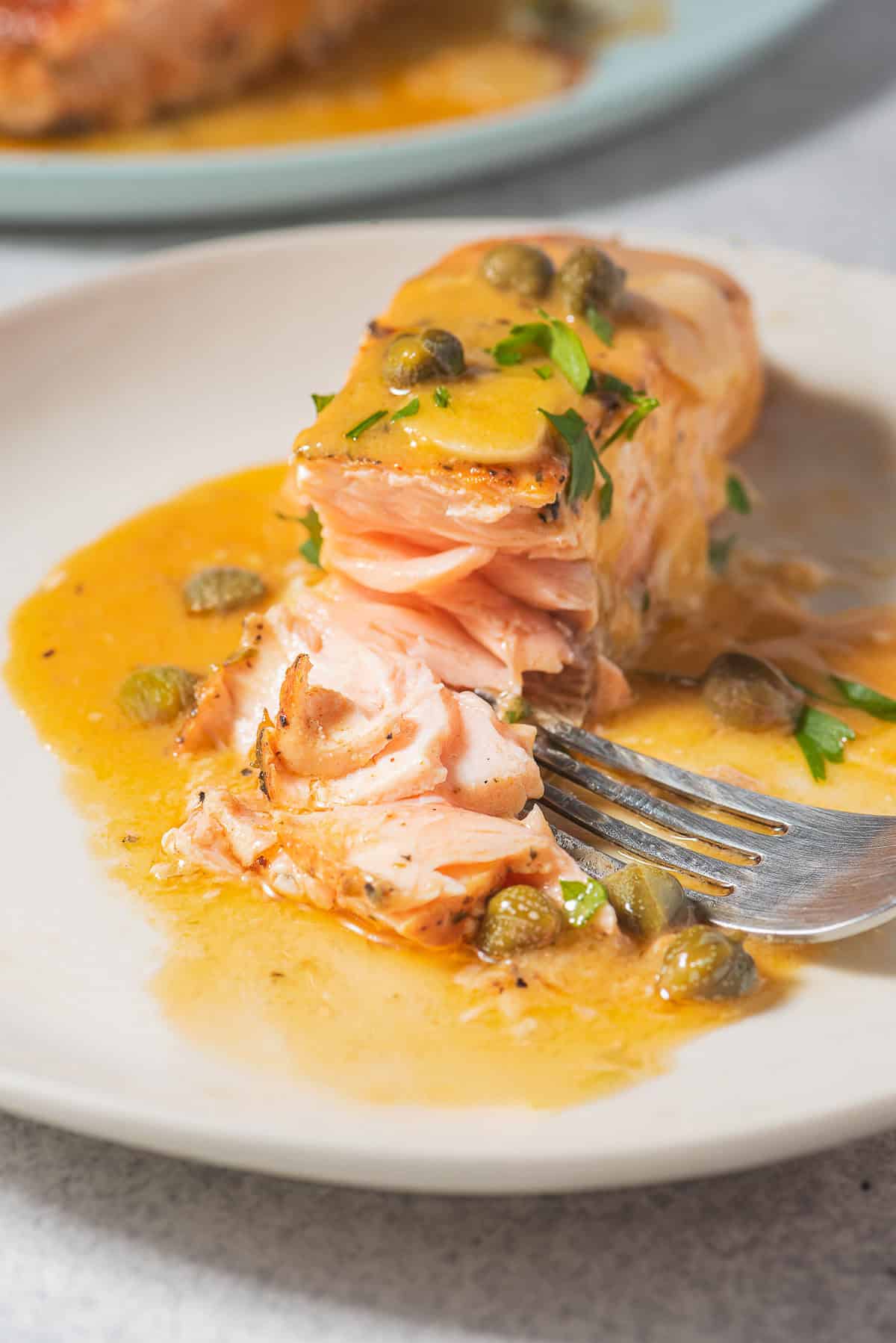 A close of a salmon piccata fillet on a plate with a fork.