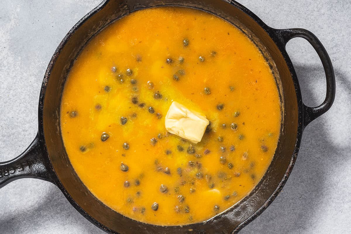 The piccata sauce with a dollop of butter in a cast iron skillet.