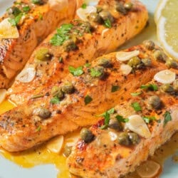 4 salmon piccata fillets on a plate with lemon wedges.