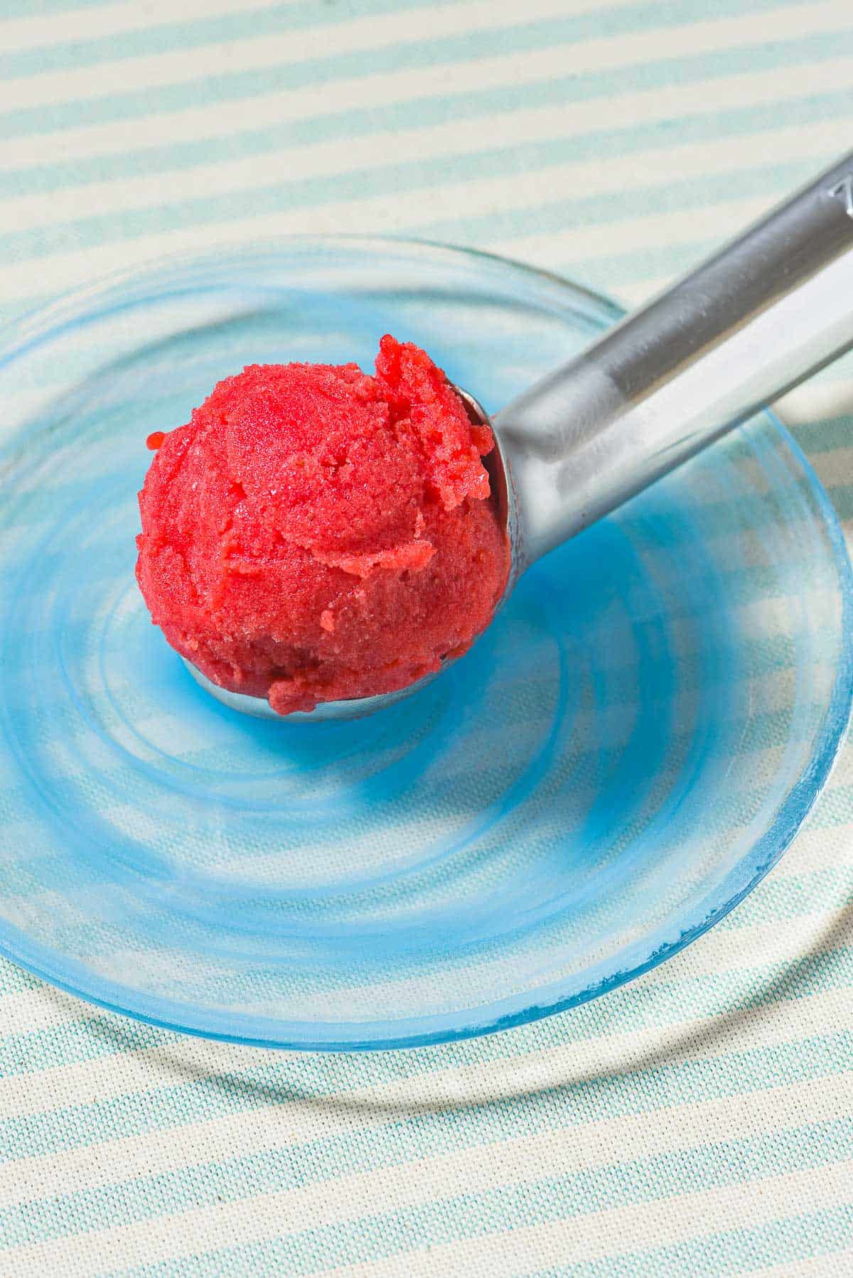 A scoop of strawberry sorbet being placed on a plate.