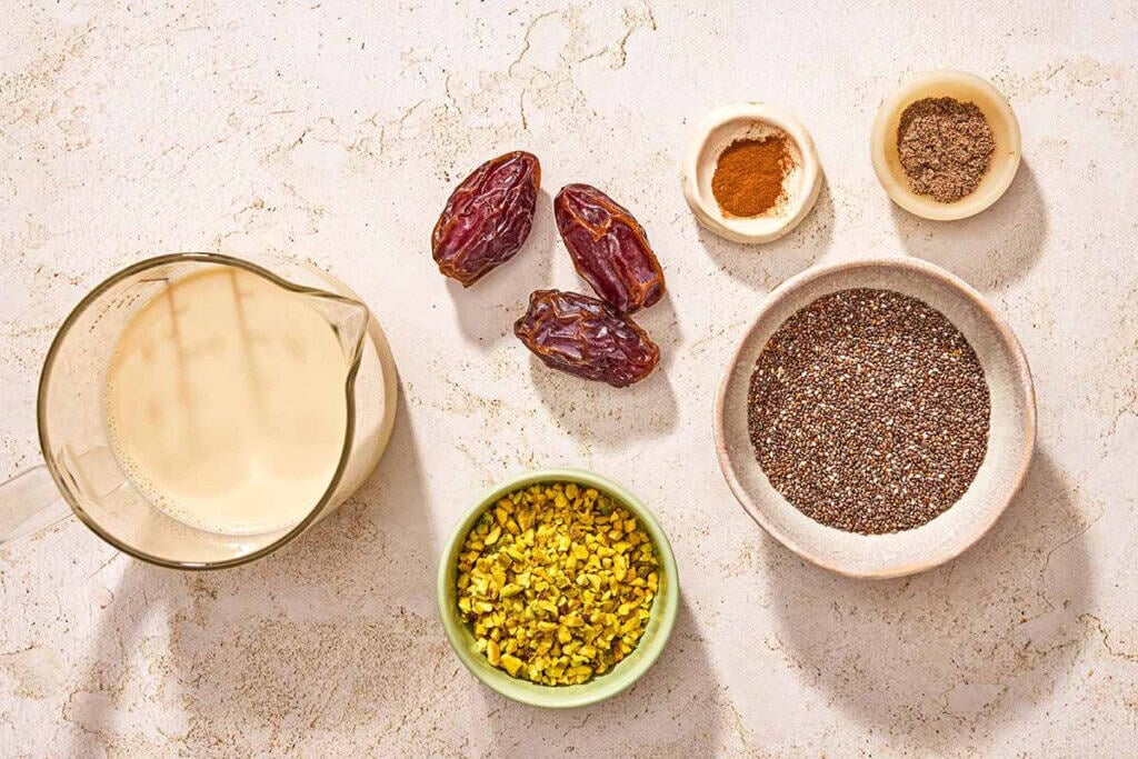 Ingredients for chia seed pudding including chia seeds, milk, dates, shelled pistachios, cardamom and ground cinnamon.