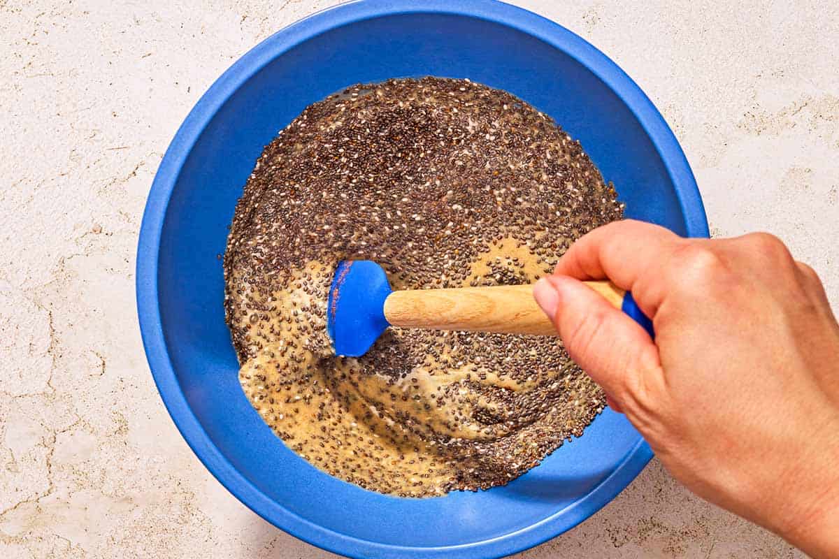 The chia seeds being stirred into the milk mixture in a bowl with a spatula.